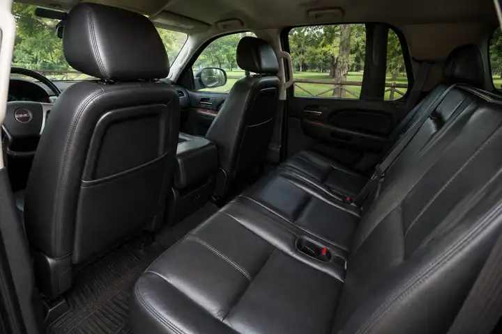 Black leather rear bench seat in a GMC SUV with front seatbacks and grab handle visible