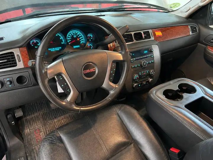 GMC SUV dashboard with illuminated gauge cluster, wood trim, center console cupholders, and black leather seating