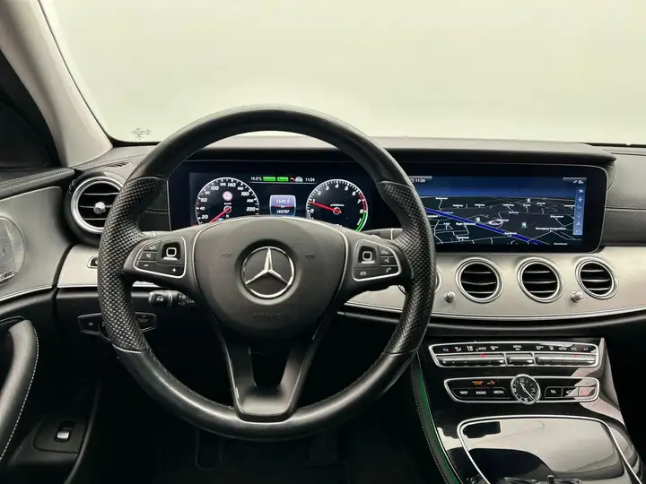 Mercedes-Benz E-Class dashboard with leather steering wheel, digital instrument cluster, and widescreen navigation display