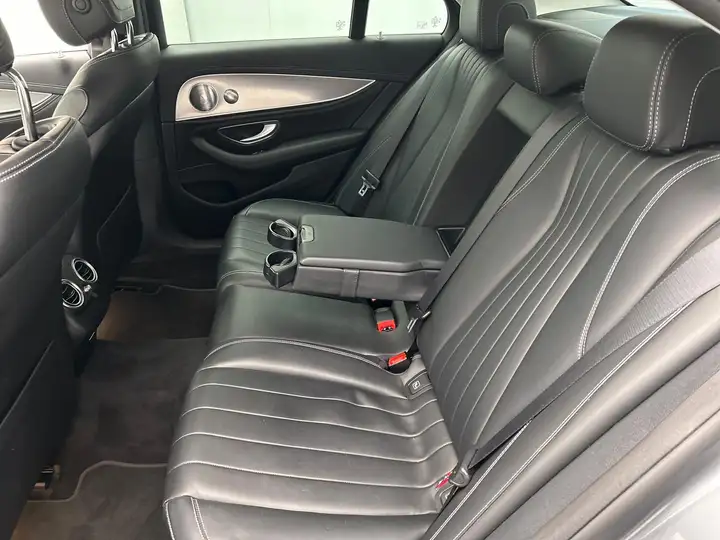 Black leather rear seat of a Mercedes-Benz E-Class with fold-down center armrest, cup holders, and rear air vents