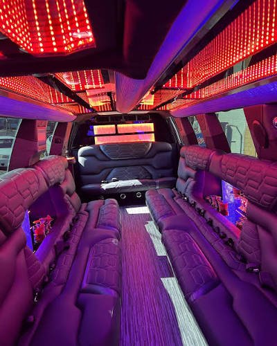 Interior of a stretch limousine with tufted leather seating, red LED ceiling lights, and a rear bench seat