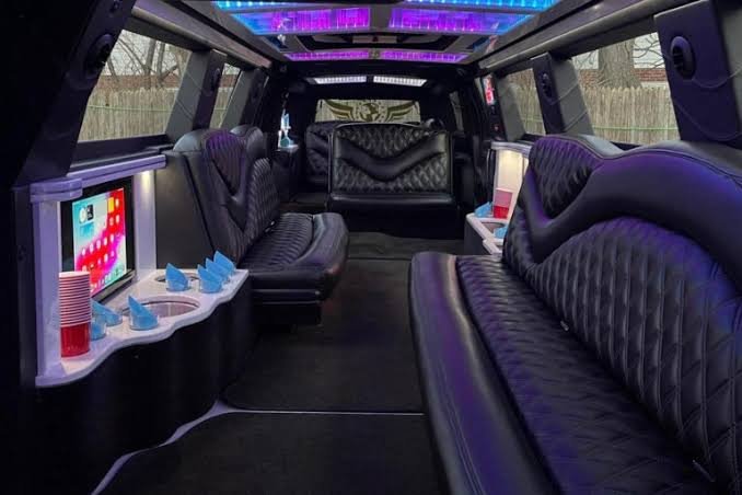 Stretch limousine interior with black diamond-stitched leather seating, a bar with cups and a built-in screen, and purple LED ceiling lights