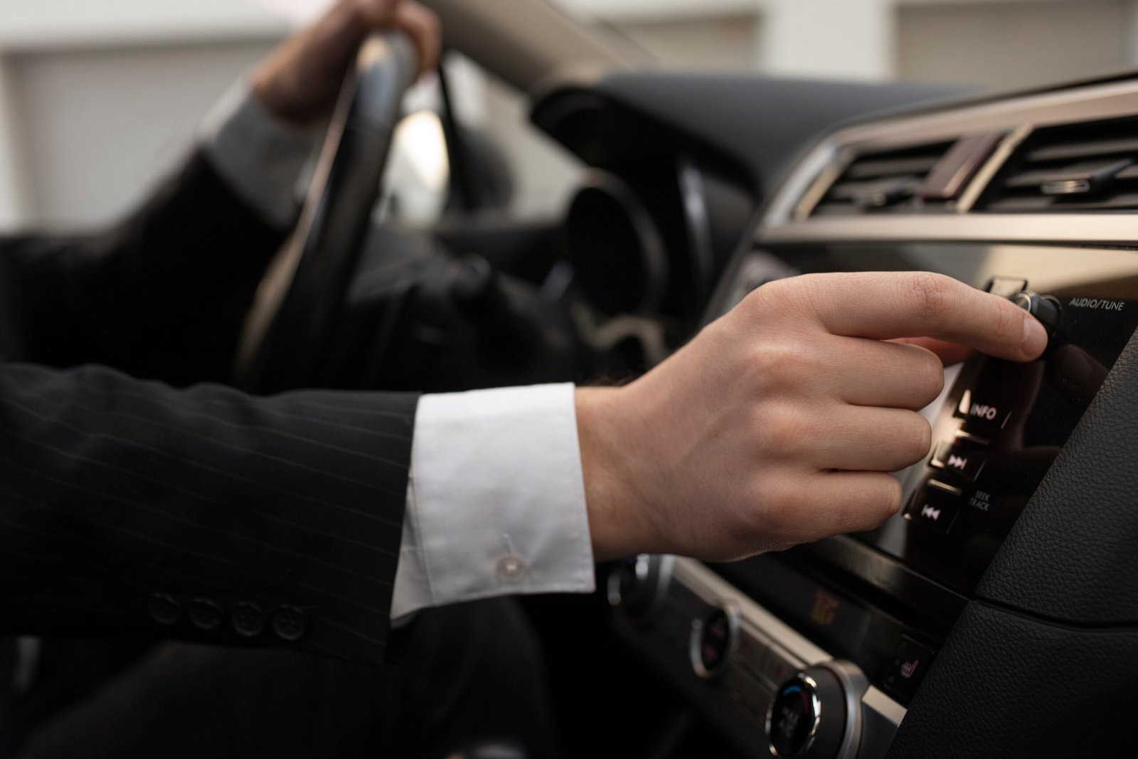 Chauffeur in suit adjusting audio controls while driving luxury vehicle