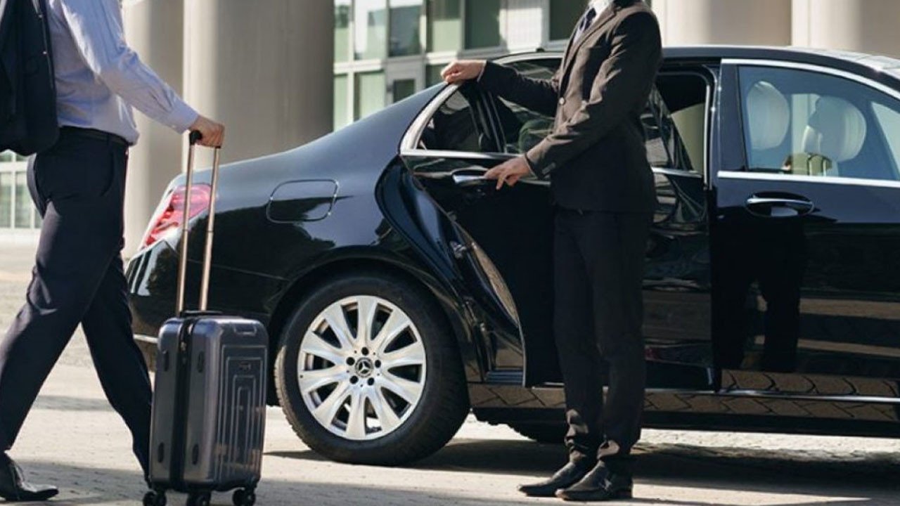 Chauffeur opening Mercedes-Benz door for business traveler with rolling luggage